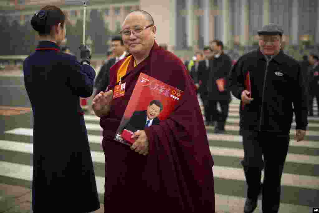 一个穿着喇嘛服装的代表在中国人民政治协商会议全体会议后离开北京人民大会堂，他携带一本《人民画报》，画报封面显示中国国家主席习近平。（2018年3月14日）