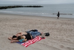 A couple lie on an American flag towel at Coney Island beach in New York during the coronavirus pandemic, May 24, 2020, during the Memorial Day holiday weekend.