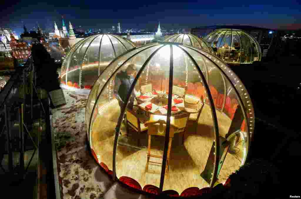 A waiter sets a table inside a transparent pod offered for private Christmas meals with backdrop of the Kremlin and Red Square on the rooftop of Ritz-Carlton hotel in Moscow, Russia, Dec. 8, 2020.