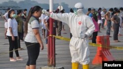 An officer wearing protective gear checks the temperature of an Indonesian migrant worker who arrived from Malaysia. 