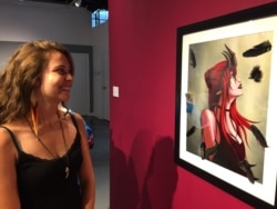 International student Erika Knecht poses with one of her favorite pieces of art, Mollyanna Sabori’s digital painting “Black Feathers,” on display at the Balzer Contemporary Edge Gallery on IAIA's campus, Santa Fe, N.M., Oct. 9, 2019. Julie Taboh/VOA
