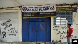 Seorang pria berdiri di dekat pintu keluar Stadion Kanjuruhan yang dihiasi tulisan grafiti tuntutan agar tragedi itu diusut tuntas, di Malang, Jawa Timur, 3 Oktober 2022. (Foto: Achmad Ibrahim/AP Photo)