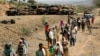 FILE - Villagers return from a market to Yechila town in south central Tigray walking past scores of burned vehicles, in Tigray, Ethiopia, July 10, 2021. 