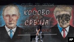 A man passes by graffiti depicting the Russian President Vladimir Putin, left, and U.S. President Donald Trump in Belgrade, Serbia, Aug. 9, 2019. The Cyrillic letters on graffiti read "Kosovo is Serbia." 