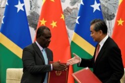 Chinese Foreign Minister Wang Yi reaches out to shake hands with Solomon Islands FM Jeremiah Manele during a ceremony to mark the establishment of diplomatic ties between the two nations, in Beijing, Sept. 21, 2019.