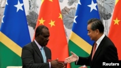 Chinese Foreign Minister Wang Yi reaches out to shake hands with Solomon Islands FM Jeremiah Manele during a ceremony to mark the establishment of diplomatic ties between the two nations, in Beijing, Sept. 21, 2019.