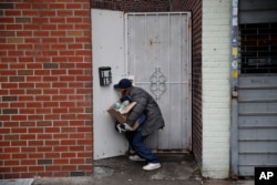 Francisco Rami­rez peers through a hole in a fence while looking for an address to deliver a box of groceries to a man in need Saturday, April 18, 2020, in the Queens borough of New York.