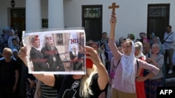 FILE - A woman's placard depicts Metropolitan Pavlo, director of the Kyiv-Pechersk Lavra monastery, standing with Russian President Vladimir Putin, as faithfuls of the Ukrainian Orthodox Church pray outside the monastery, in Kyiv, July 4, 2023.