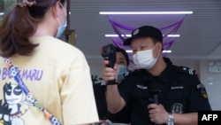 A security guard checks the body temperature of a woman in Wuhan in China's central Hubei province, May 11, 2020. 