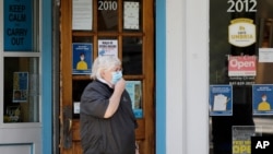 FILE - A woman wears mask as she walks past an "open" sign cafe in Evanston, Ill., May 29, 2020. 