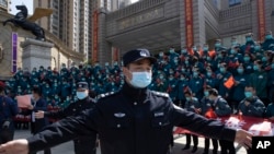 FILE - A policeman moves journalists back from an event held for the last group of medical workers who came from outside Wuhan to help the city during the coronavirus outbreak, in Wuhan, China, April 15, 2020. 