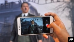 Pengunjung menggunakan ponsel untuk mengambil foto lilin angka Adolf Hitler berlatar belakang kamp Auschwitz-Birkenau di Mata De Museum, Yogyakarta, Indonesia, 8 November 2017. (Foto: dok). Kelompok HAM mengecam menyebutnya "memuakkan" dan menuntut tampilan ini agar segera disingkirkan.