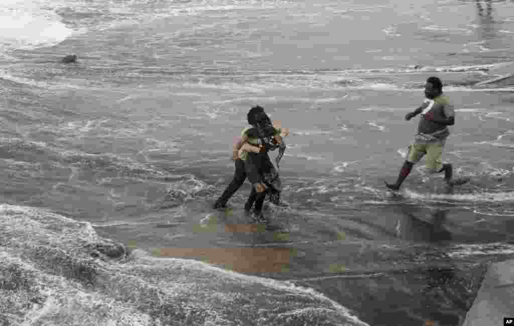 A man, right, rushes to help as another rescues a woman who fell due to strong tidal waves on the Bay of Bengal coast at Gopalpur, Orissa, Oct. 12, 2014.