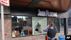 پلیس مینیاپولیس در حال عکسبرداری از فروشگاهی که پنجره آن به دلیل اصابت گلوله شکسته است