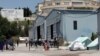 FILE - Migrants walk inside a new refugees camp in an abandoned factory in Derveni, a north suburb of Thessaloniki, May 27, 2016.