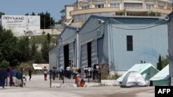 FILE - Migrants walk inside a new refugees camp in an abandoned factory in Derveni, a north suburb of Thessaloniki, May 27, 2016.