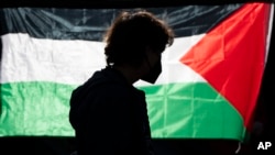 La silueta de un alumno de la Universidad de Oregon se ve ante una bandera palestina en un campamento de carpas levantado en la universidad como protesta por la guerra entre Hamás e Israel, el 29 de abril de 2024 en Eugene, Oregon. 