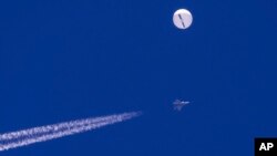 FILE - Balon besar dan pesawat jet tempur dengan ekor putihnya (contrail) terlihat melayang di atas Samudra Atlantik, tepat di lepas pantai South Carolina, Sabtu, 4 Februari 2023. (Chad Fish via AP)