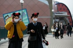 Two visitors with masks and Minnie Mouse ear headbands leave Tokyo Disneyland in Urayasu, near Tokyo, Feb. 28, 2020.