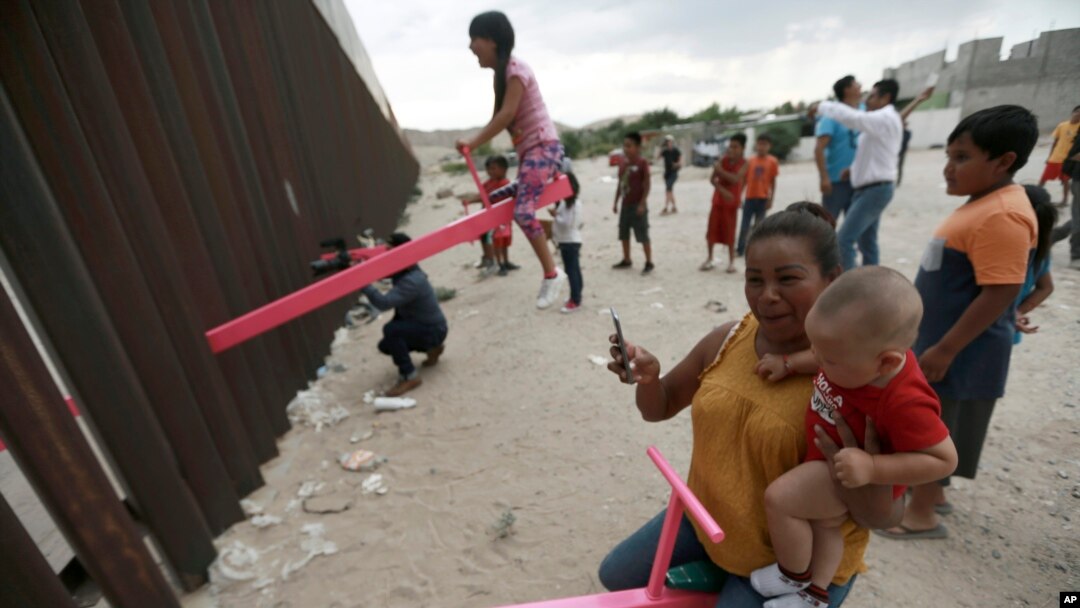 A mother and her baby play on a seesaw installed between the steel fence that divides Mexico from the United States in Ciudad de Juarez, Mexico, July 28, 2019. 