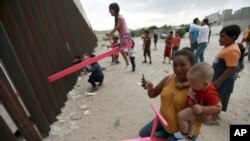 A mother and her baby play on a seesaw installed between the steel fence that divides Mexico from the United States in Ciudad de Juarez, Mexico, July 28, 2019. 