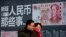 一對青年男女走過北京街頭宣傳中國新版人民幣100元鈔票的廣告牌。（2016年1月11日） 