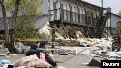 Mahasiswi beristirahat di depan gedung apartemen yang hancur akibat gempa bumi di kota Minamiaso di prefektur Kumamoto, Jepang selatan (16/4). 