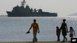 FILE - A Filipino family stroll the beach at Subic Bay as the USS Harpers Ferry approaches to dock.