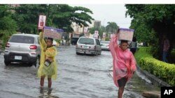 FILE - Women walk along a flooded street after a heavy downpour in Lagos, Nigeria, on July 10, 2024.