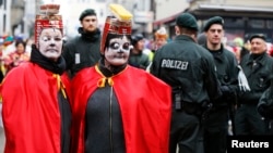 FILE - German police officers stand guard as two carnival revelers wait for the start of the traditional Rose Monday carnival parade in the western German city of Cologne, Feb. 16, 2015.