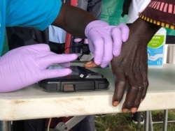 A woman's fingerprints are scanned before receiving a cash voucher at the Lobule refugee settlement in Uganda. August 14, 2019 (T. Krug/VOA)