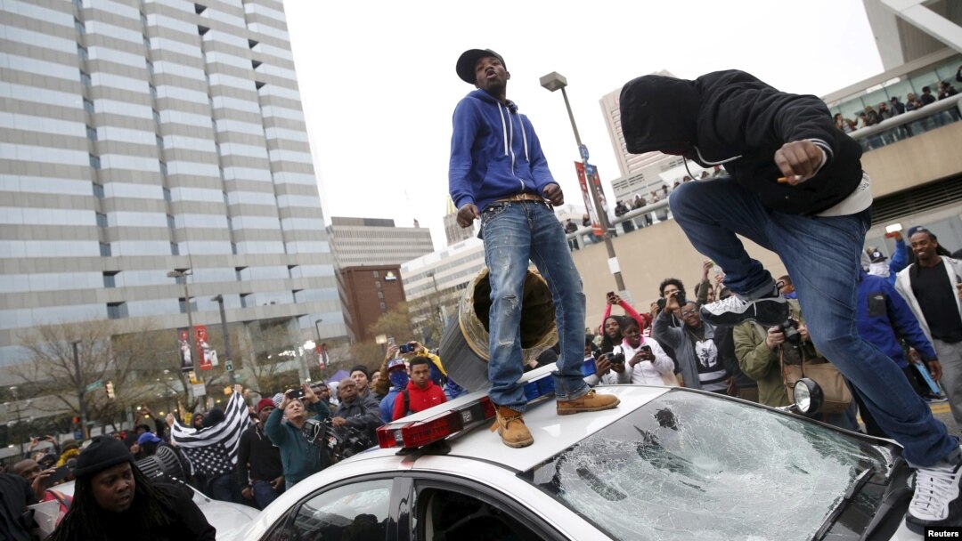 Para demonstran melompati dan merusak mobil polisi dalam aksi protes rusuh di Baltimore, Sabtu (25/6).