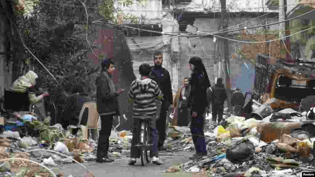 Civilians stand along a street amid garbage and rubble of damaged buildings in the besieged area of Homs, Jan. 27, 2014. 