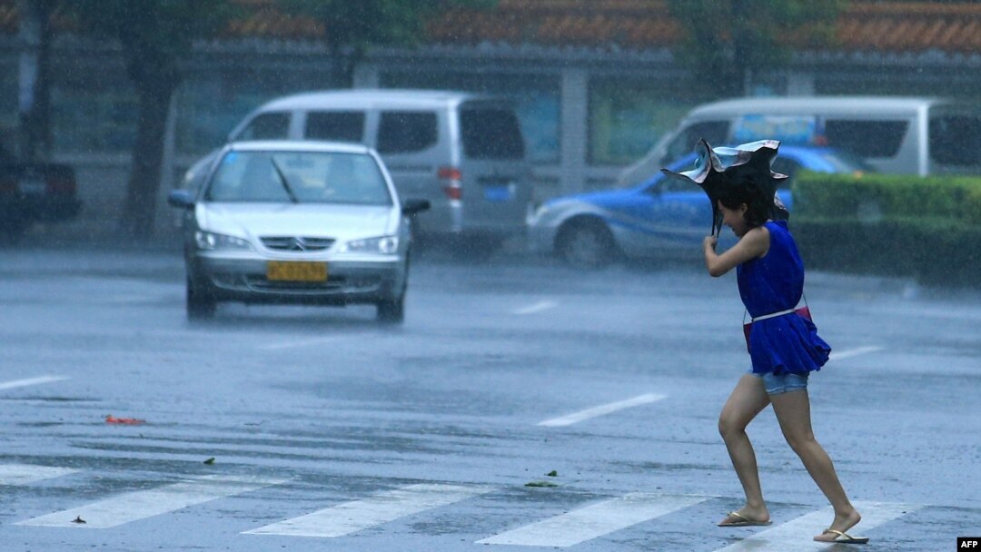 Seorang perempuan menyeberang japan saat human lebat dan angin kyat melanda Haikou, provinsi Hainan di China Selatan (18/7).