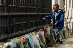 A young boy places a flower on the gate at Buckingham Palace in London, after the announcement of the death of Britain's Prince Philip, April 9, 2021.