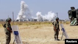 Turkish soldiers stand guard near the Mursitpinar border gate in Suruc in Sanliurfa province as smoke rises in the Syrian town of Kobani in the background, June 27, 2015. 