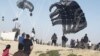 This image grab from an AFPTV video shows Palestinians running toward parachutes attached to food parcels, air-dropped from US aircrafts on a beach in the Gaza Strip on March 2, 2024.