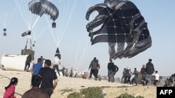 This image grab from an AFPTV video shows Palestinians running toward parachutes attached to food parcels, air-dropped from US aircrafts on a beach in the Gaza Strip on March 2, 2024.