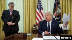 El secretario de Justicia de EE.UU., William Barr, observa de pie al presidente Donald Trump mostrando unos papeles durante una conversación con periodistas en la Sala Oval de la Casa Blanca, el 28 de mayo de 2020.