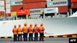 FILE - Workers stand in line next to a container ship at a port in Qingdao in China's eastern Shandong province, April 8, 2018.