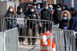 Patients wearing face masks and personal protective equipment wait on line for COVID-19 testing outside Elmhurst Hospital Center, March 27, 2020, in New York.