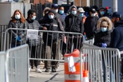 FILE - Patients wearing face masks and personal protective equipment wait on line for COVID-19 testing outside Elmhurst Hospital Center, March 27, 2020, in New York City.