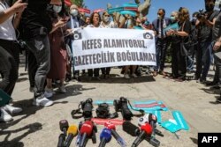 FILE - Reporting equipment lies on the ground outside the offices of Ankara’s government, and protesters hold a banner that reads "We can’t breathe. Journalism cannot be drowned” during a rally calling for journalists to be protected from police, June 29, 2021.