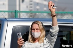 A woman waves from outside Daikoku Pier Cruise Terminal as she communicates via phone with a passenger on the cruise ship Diamond Princess, as the vessel's passengers continue to be tested for coronavirus, in Yokohama, Japan, Feb. 13, 2020.