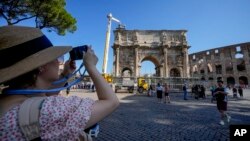 A tourist takes photos of the Arch of Constantine in Rome, Sept. 4, 2024, as workers gather fragments and secure broken areas of the arch after lightning struck it during a storm the day before, loosening fragments from the ancient Roman structure.