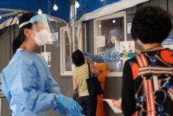 A medical worker in a booth takes a nasal sample from a woman during coronavirus testing at a makeshift testing site in Seoul, South Korea, July 28, 2021.