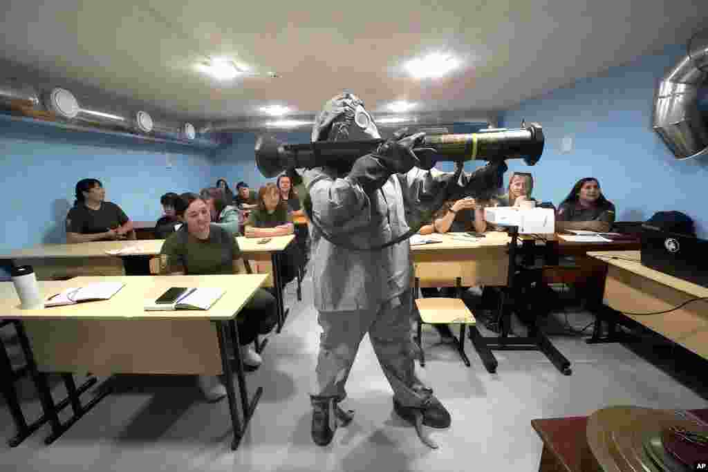 A Ukrainian serviceman in a protective suit demonstrates a grenade launcher to women during a training course for national resistance for local population in Kharkiv region, Ukraine.