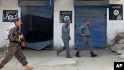 FILE - Afghan police walk past Islamic State militant flags on a wall, after an operation in the Kot district of Jalalabad province east of Kabul, Afghanistan, Aug. 1, 2016. U.S. military officials said Friday that top Islamic State official Abu Sayed was killed July 11 in an airstrike on the group's headquarters in the northeastern Afghan province of Kunar.