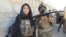 An Afghan National Army soldier and VOA reporter Ayesha Tanzeem, left, wait at a police checkpoint barrier in Achin, a district in eastern Afghanistan.