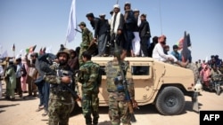 Para militan Taliban Afghanistan dan warga berdiri di kendaraan lapis baja milik Tentara Nasional Afghanistan merayakan gencatan senjata pada hari ketiga Idul Fitri, di Distrik Maiwand, Provinsi Kandahar, 17 Juni 2018. (Foto: Javed Tanveer/AFP)